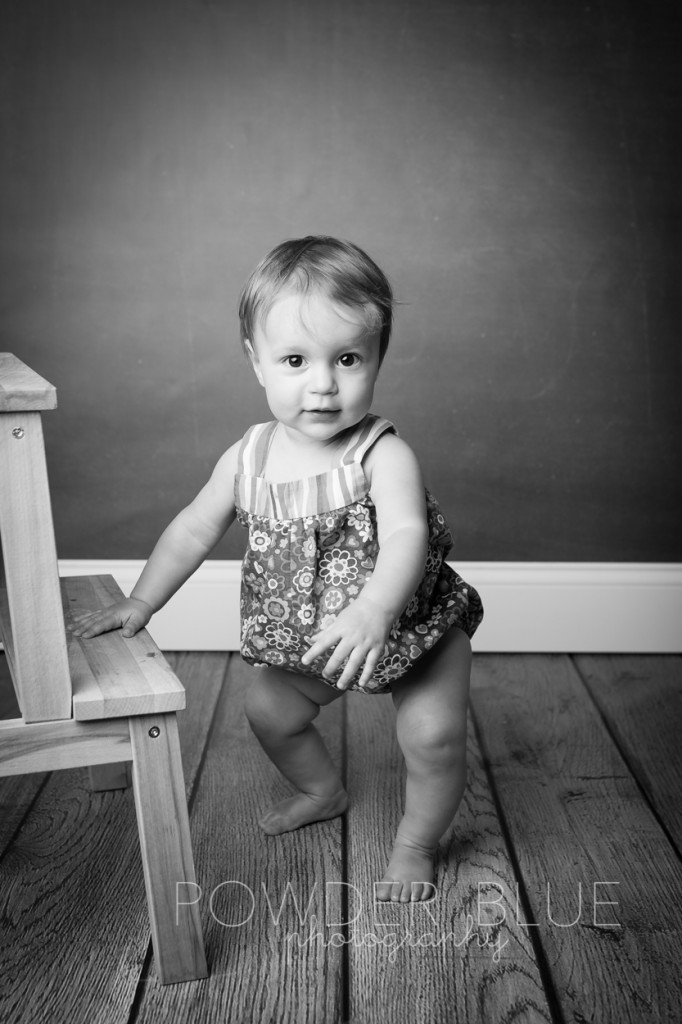 10 month old baby girl in portrait studio with black chalkboard backdrop standing up