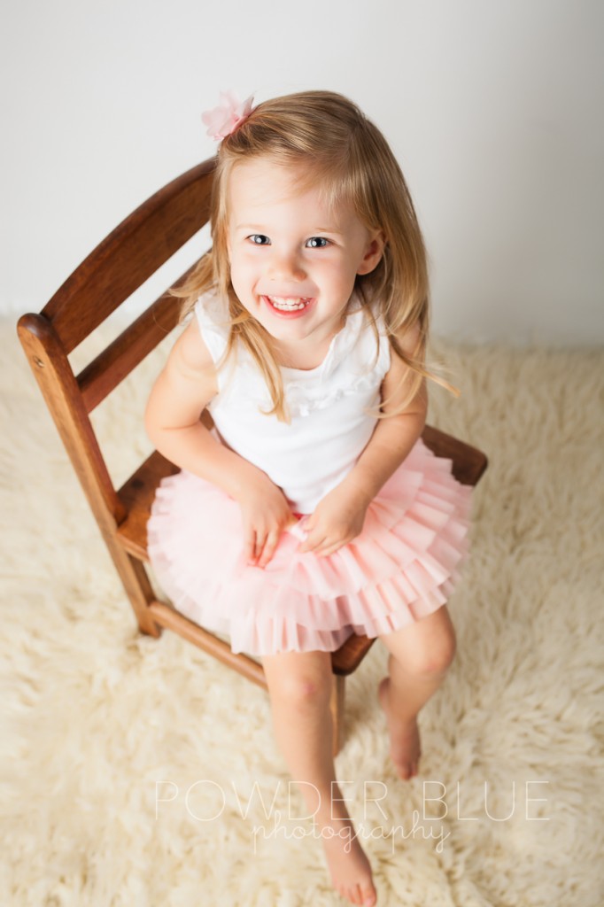 two year old toddler sitting on a chair smiling pink hair flower studio portrait© 2013 Powder Blue Photography. www.powderbluephoto.com